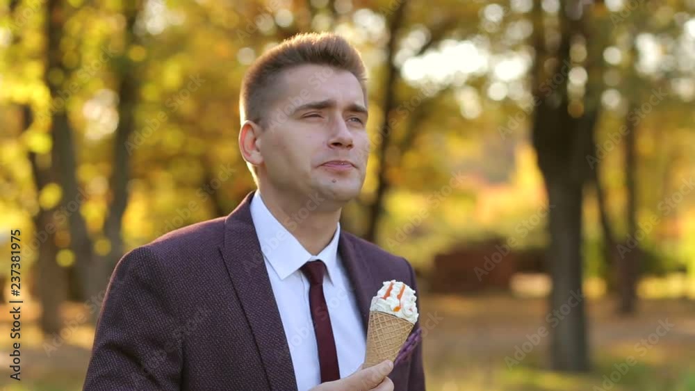 Successful young businessman walks in the autumn Park and eats ice cream. Modern man in a business suit in Park with ice cream and enjoys the warm weather. Successful young businessman walks in the autumn Park and eats ice cream. Modern man in a business suit in Park with ice cream and enjoys the warm weather.