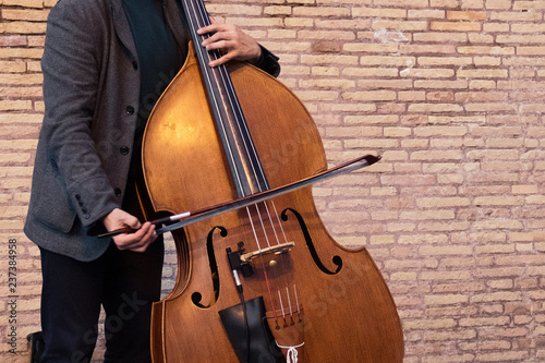A street artist playing a cello on the street in front of a brick wall.