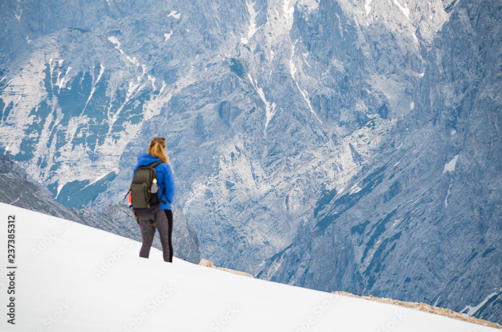 Young beautiful woman walking in the snow on top of a mountain with a huge mountain in the distance