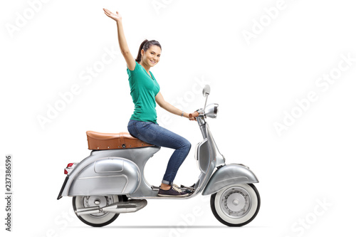 Young female riding a vintage scooter and waving