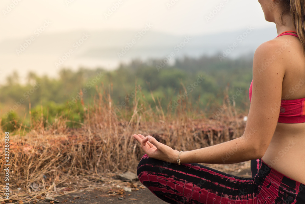 Girl sitting and meditating in front of a sunset