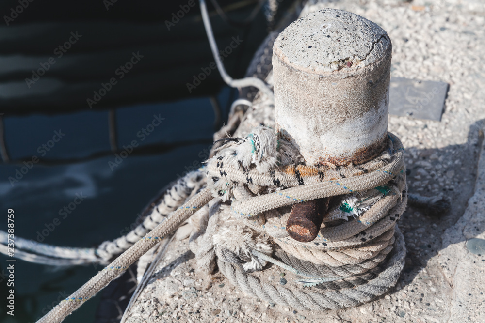 Mooring bollard with tied naval ropes stands on concrete pier