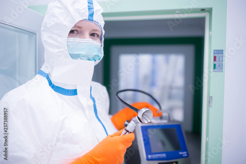 Lab technician wearing cleanroom overall holding apparatus at material sluice