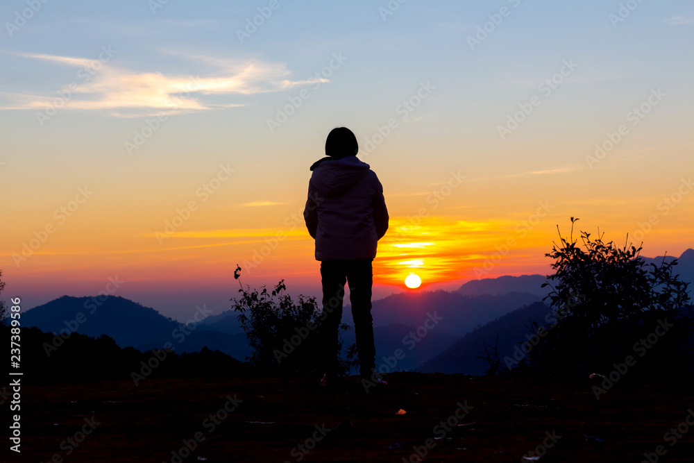 Silhouettes of young girl looking morning sunrise on peak of mountain.
