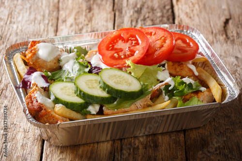 Takeaway Dutch kapsalon from french fries, chicken, fresh salad, cheese and sauce in a close-up foil tray. horizontal