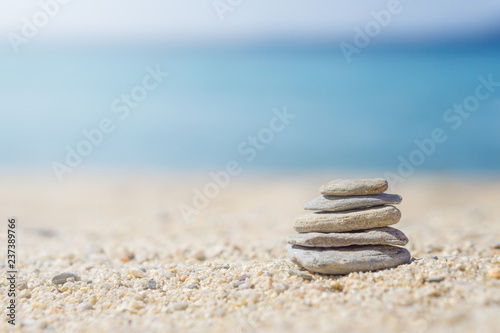 Vertical ordered stones on sand at the beach. Blurred blue sea at background