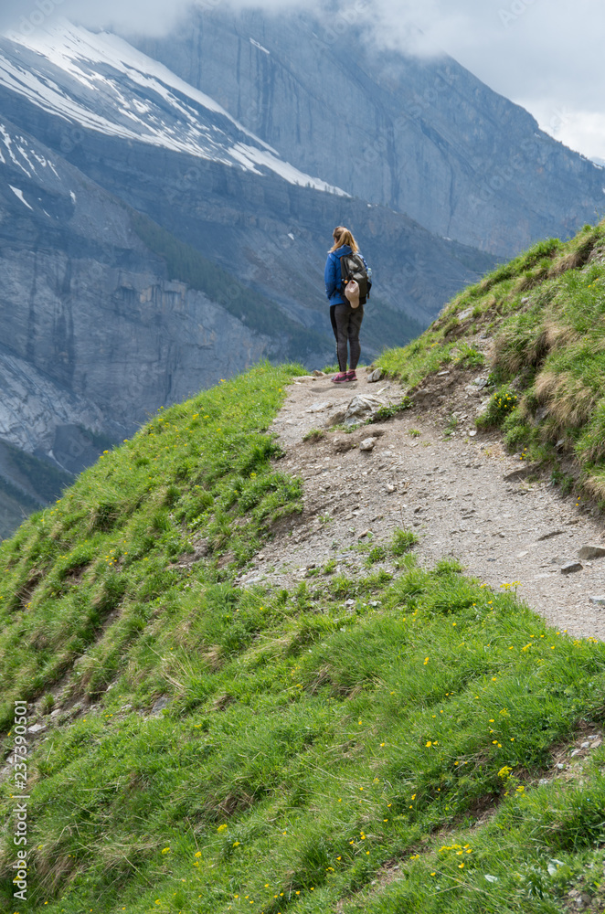 Young beautiful woman standing on a mountain path looking out over the range