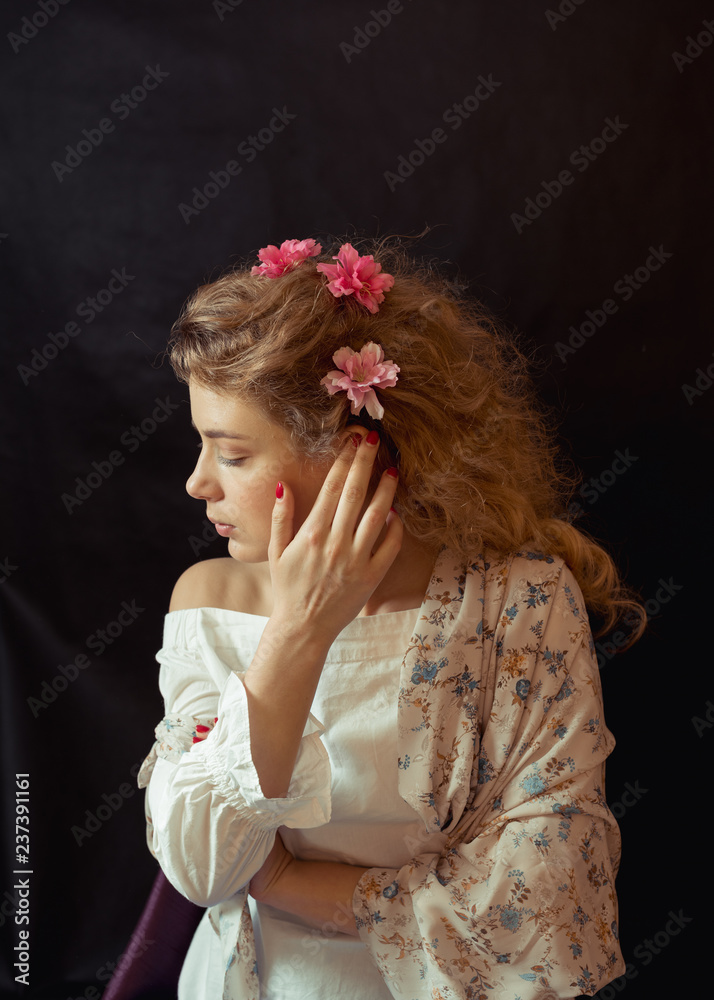 Fototapeta premium Portrait of a young romantic woman with blond curly hair in a vintage floral dress sitting over black background. Close Up of woman