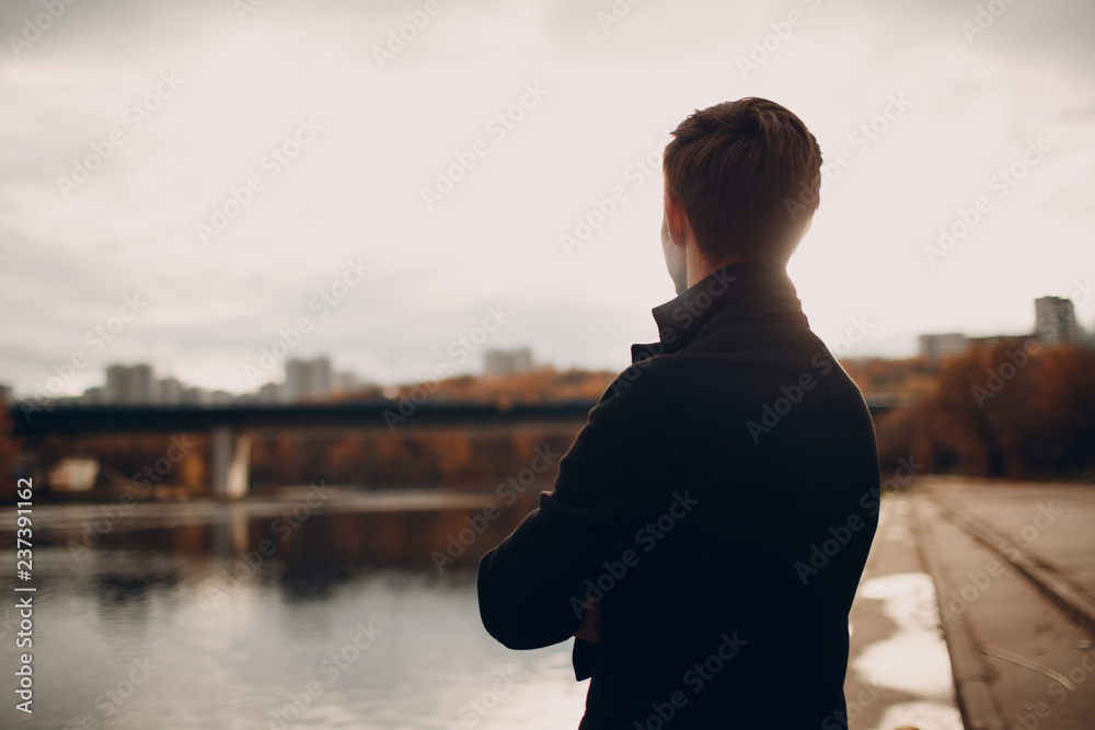 The man on the river embankment looks at the houses and the bridge in front of them.