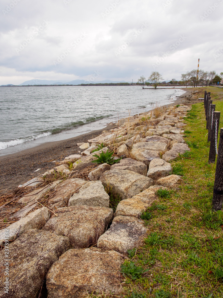 Wide vertical view of the stony and grassy shores of Lake Biwa on a stormy spring day. Nagahama, Shiga, Japan. Travel and tourism.