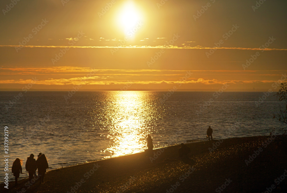 Evening sunset on the background of sea water and people walking along the beach