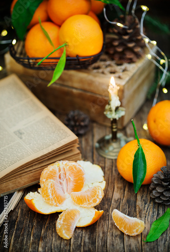 Tangerines with liaves and books on wooden background with burning candle, pine cones and Christmas tree. photo