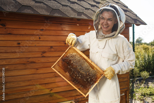 Young female beekeeper hold wooden frame with honeycomb. Collect honey. Beekeeping concept