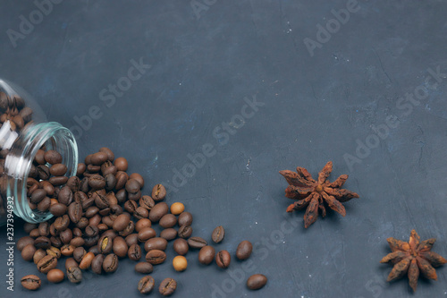 roasted coffee beans poured from a glass jar. angular placement of the coffee object. on dark concrete. horizontal view. copy space