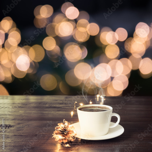 Cup of black coffee on wooden table in cafe. Christmas lights and gold garland on background.