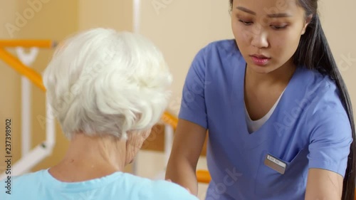 Wallpaper Mural Medium shot of young female physical therapy specialist talking and checking flexibility of arm of senior woman Torontodigital.ca