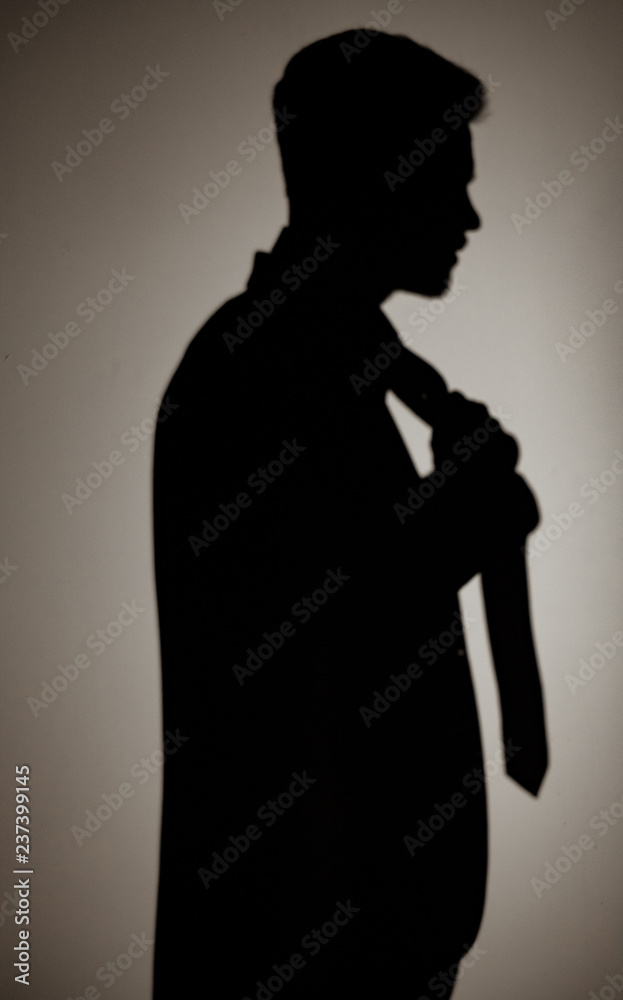 Man's shadow on the wall in a suit is straightening his tie.