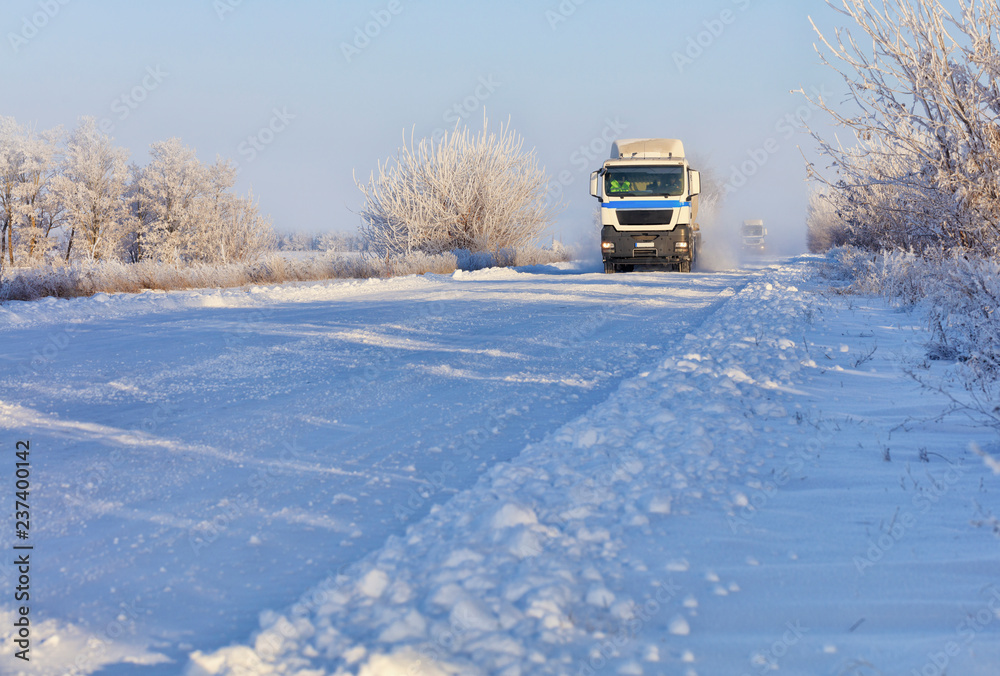 A convoy of heavy trucks drives along a snowy white road.
