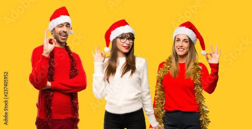 A group of people Blonde woman dressed up for christmas holidays showing an ok sign with fingers on yellow background