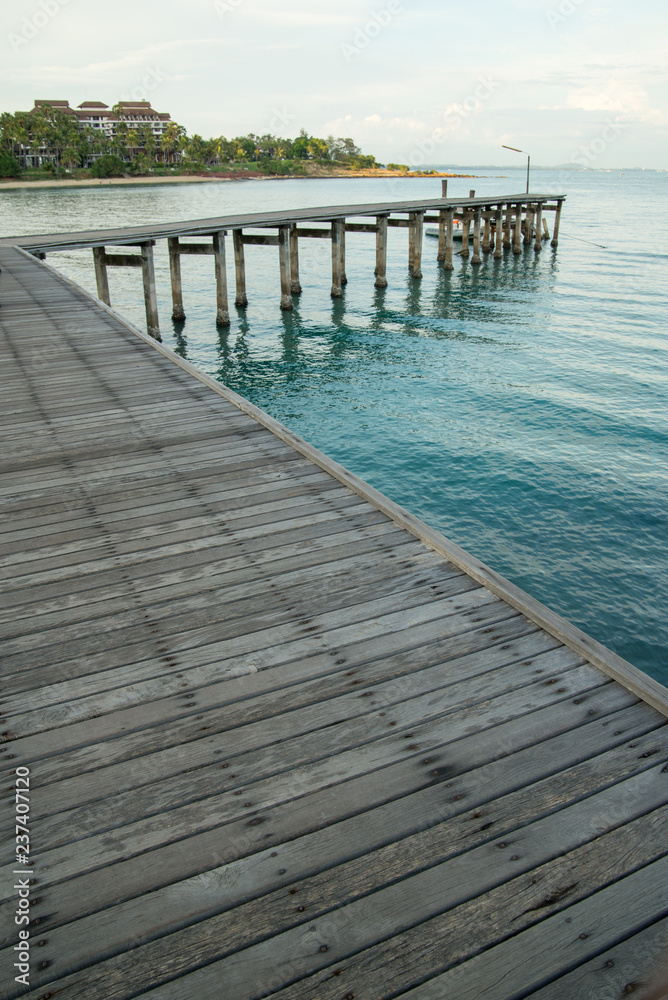 Wide-angle detail of a long wooden pier over still blue ocean waters, islands in the background. Vertical orientation. Khao Laem Ya, Rayong, Thailand.