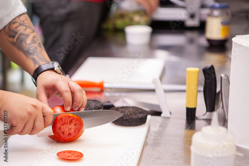 Chef slicing tomatoes for burger in kitchen restaurant