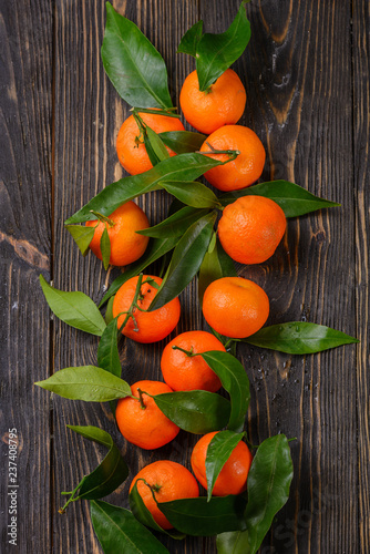 Ripe organic clementines or tangerines with leaves over dark wooden plank table as background. Top view, space. Healthy eating