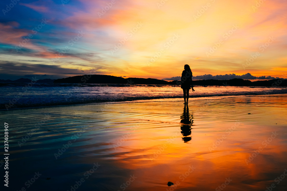 single girl enjoying herself with background of dramatic evening glow during sunset, photo taken on Ao Nang beach, Krabi, Thailand.