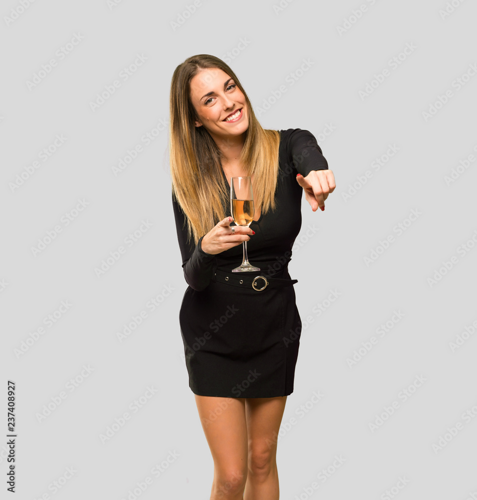 Woman with champagne celebrating new year 2019 points finger at you while smiling on isolated grey background Woman with champagne celebrating new year 2019 points finger at you while smiling on isolated grey background