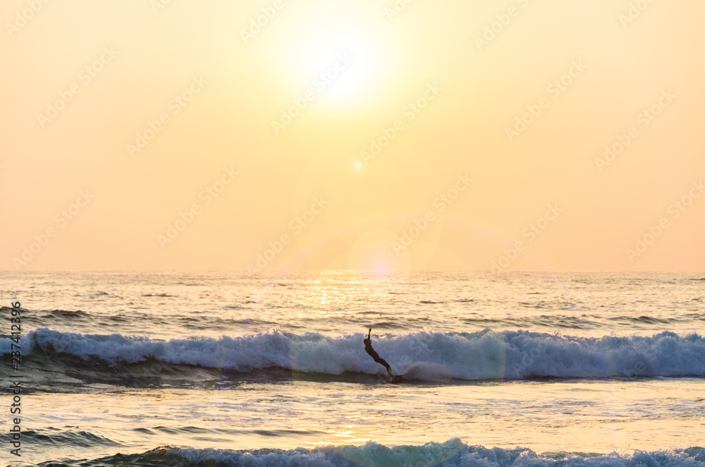 Obraz premium Surfing at Sunset. Young Man Riding Wave at Sunset. Outdoor Active Lifestyle.