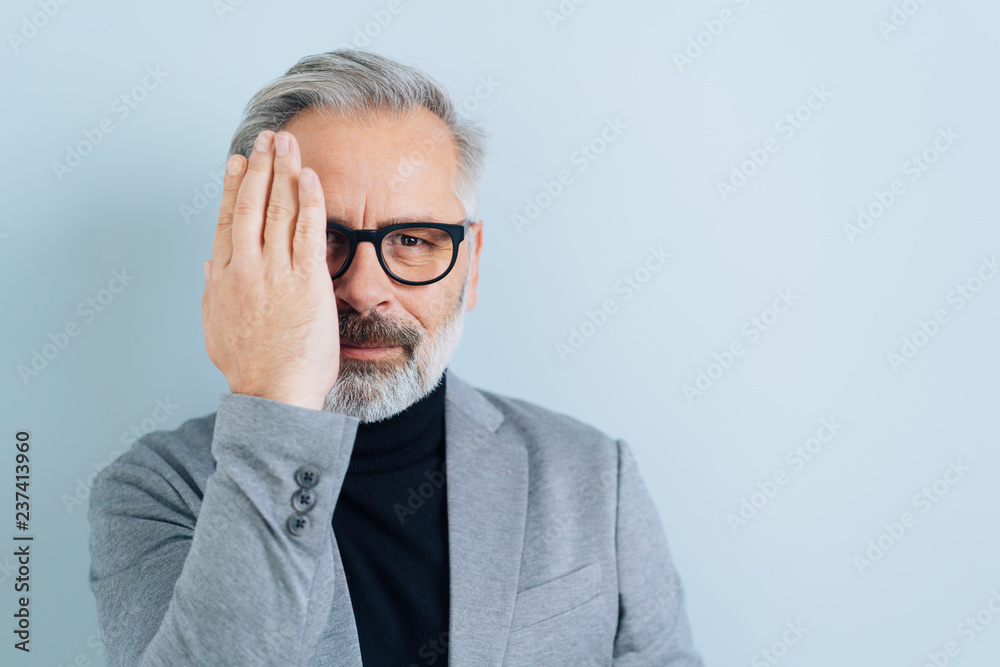 Middle-aged man covering one eye with a hand Middle-aged man covering one eye with a hand