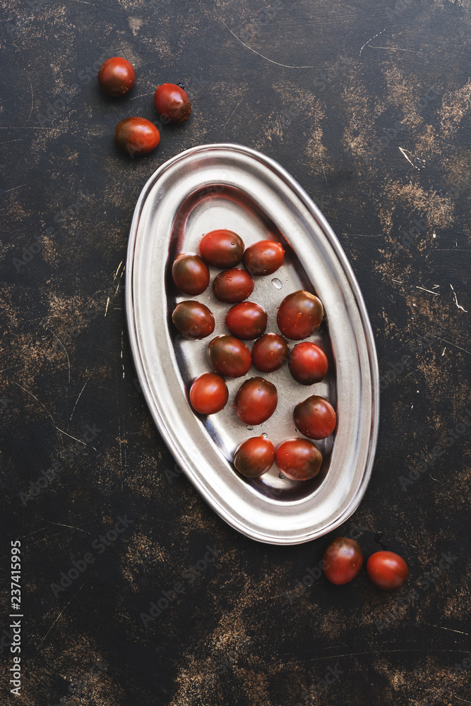 Black cherry tomato in a metal dish on a dark rustic background. Top view, flat lay. Black cherry tomato in a metal dish on a dark rustic background. Top view, flat lay.