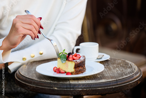 Cake with cream delicious dessert. Appetite concept. Dessert cake cup of coffee and female hand with fork close up. Piece of cake with red berry. Gourmet recipe food. Cake slice on white plate
