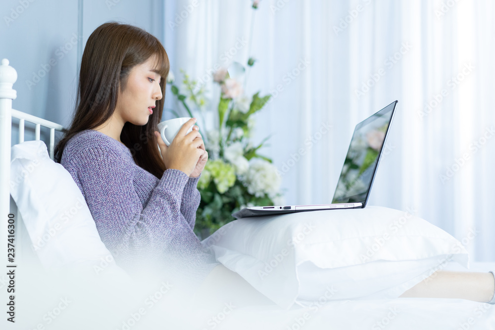 Asian woman working on bed .She dress sweater violet colour.Morning check email internet from notebook. Asian woman working on bed .She dress sweater violet colour.Morning check email internet from notebook.