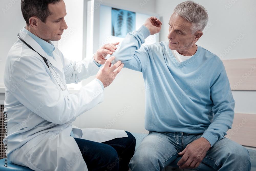 Attentive physician examining sick arm Attentive physician examining sick arm
