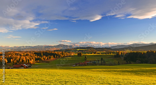 Beautiful colorful evening mood in the Allgaeu region (Bavaria, Germany) in autumn. Rural landscape with meadows, forests and farms. Mountains (Allgaeu Alps) in the background.