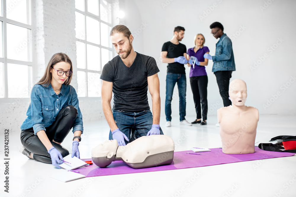 Fototapeta premium Group of young people practising to make artificial breathing with medical dummies during the first aid training in the white room
