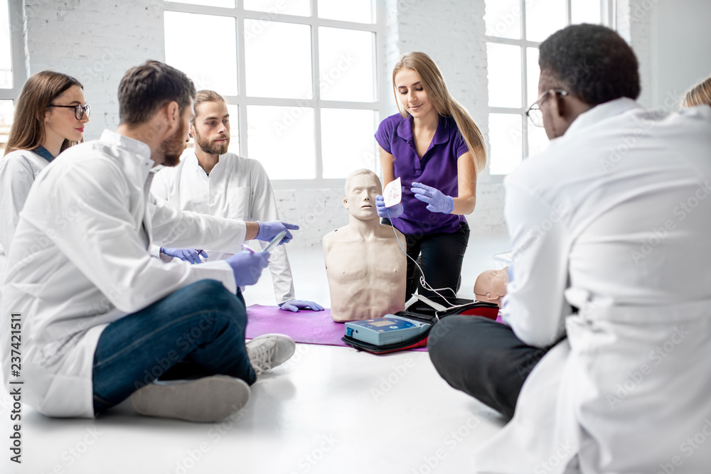 Group of young medics with instructor shows how to do defibrillation on the dummy during the first aid training indoors