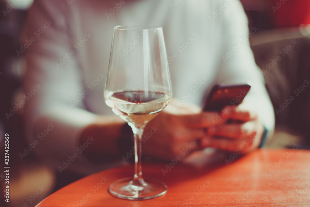 Man with a glass of white sparkling wine and  mobile phone - hands of a man distracted by social on his smartphone - focus on glass