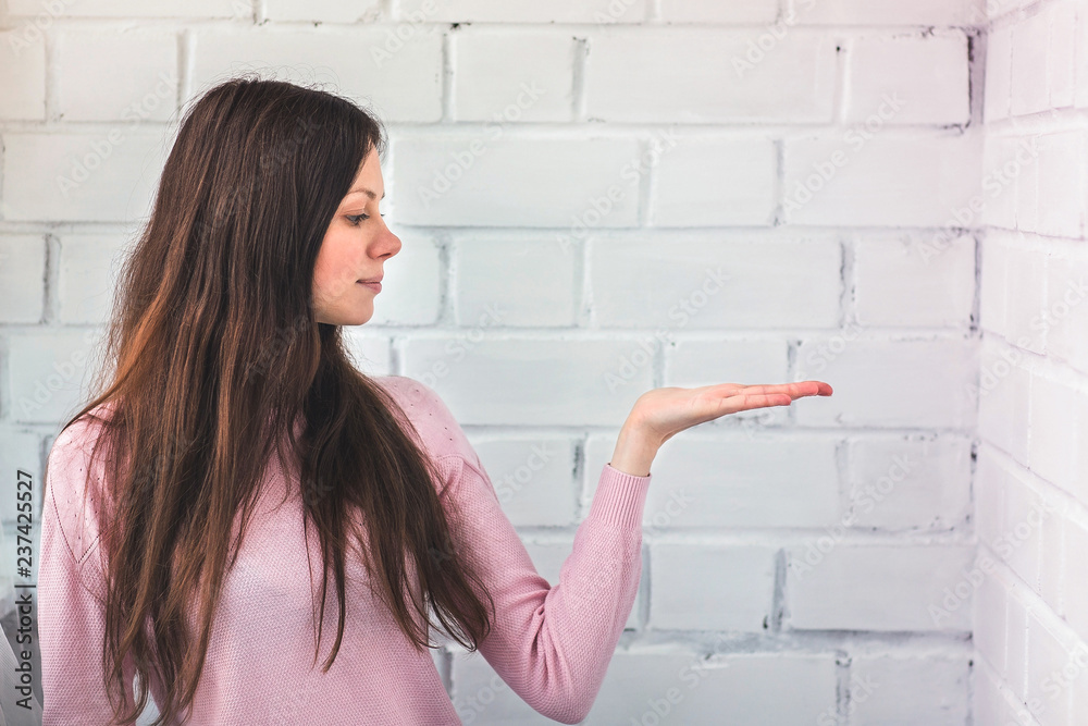 Beautiful woman stands a white brick background and keep on something on her hand and look on it. Beautiful woman stands a white brick background and keep on something on her hand and look on it.