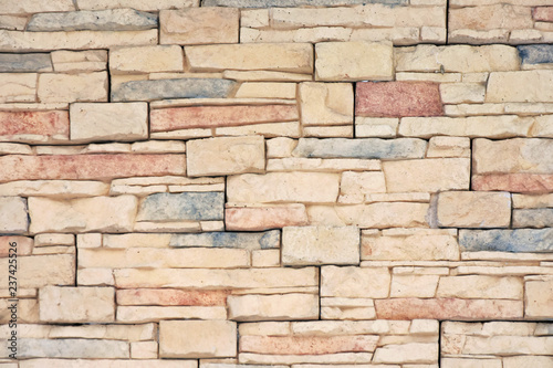 Background with old brick wall of aged beige and colorful bricks. Natural stone surface with rough texture and selective focus. Decorate abstract wallpaper with structure granite rocks.