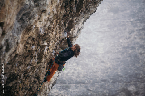 woman climbs grey-color rock in orange pants