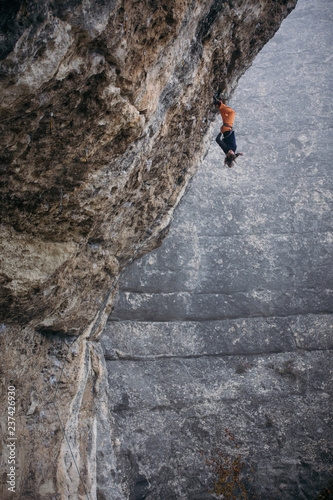 woman-climber hangs upside-down in a grey-color rock in orange pants