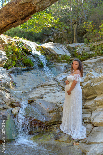 pregnant girl in dress near a waterfall in the summer