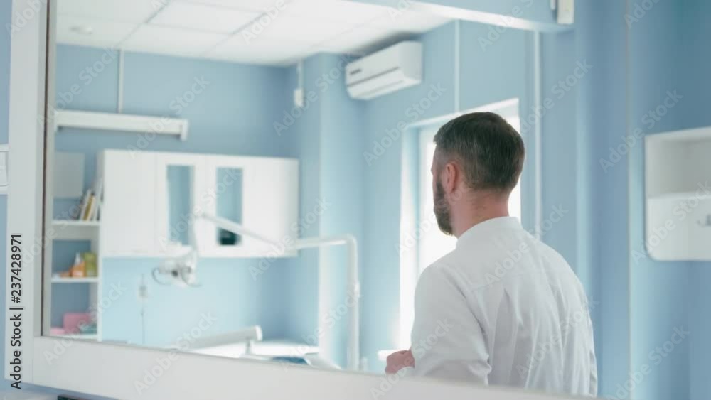 Confident Bearded Doctor is Preparing to Work and Putting on his Lab Coat Robe Looking at Mirror Confident Bearded Doctor is Preparing to Work and Putting on his Lab Coat Robe Looking at Mirror