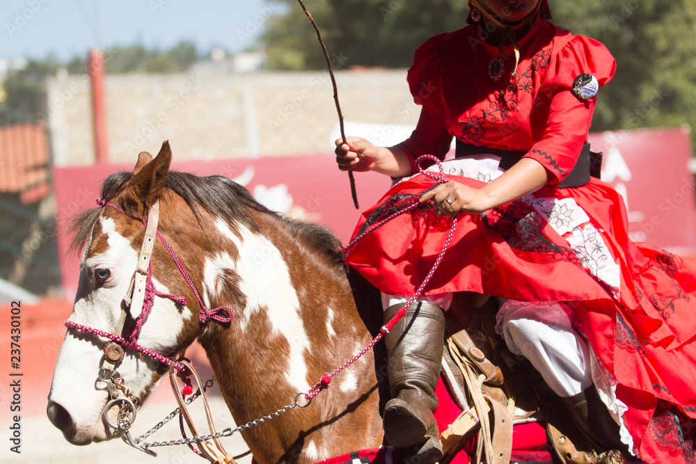 A mexican escaramuza with red dress riding a brown horse