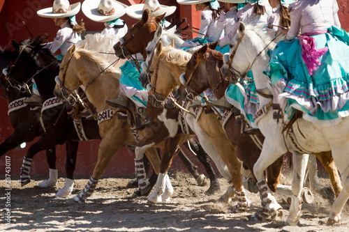 Group of mexican escaramuza girls with mexican dresses and sombrero riding horses in a line formation