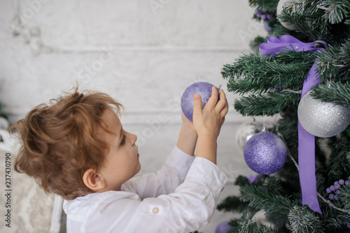 lateral view of a 6-year blond boy decorating a christmas tree with puprple toys photo