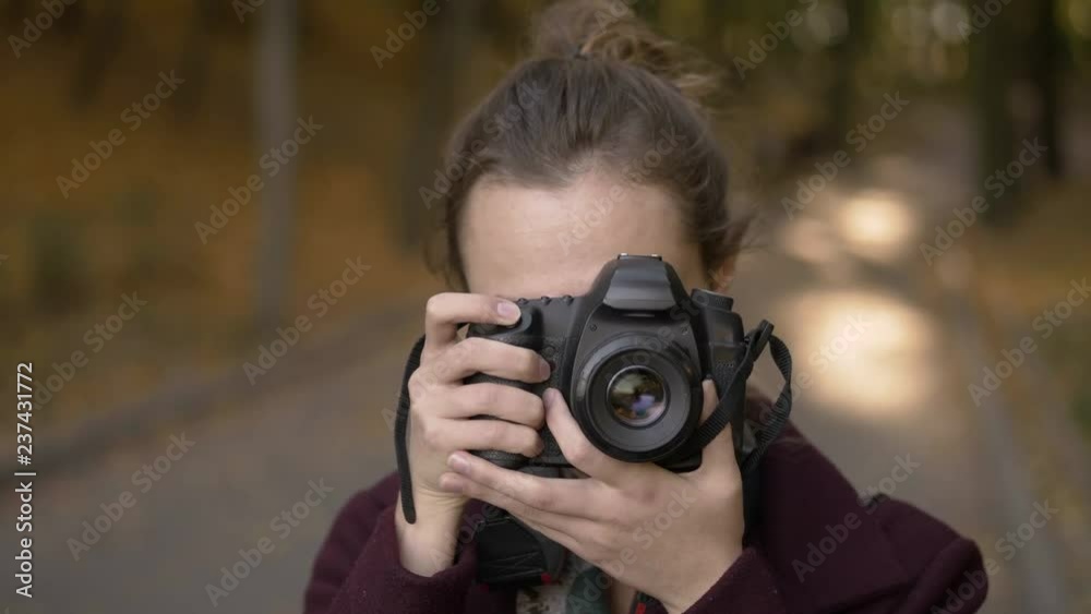 Professional young woman photographer with digital camera taking pictures at autumn city park. Close up, slow motion, shallow depth of field.