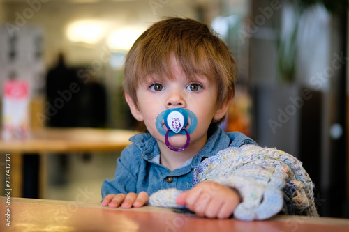18 month old baby boy sat in high chair with dummy and comfort blanket