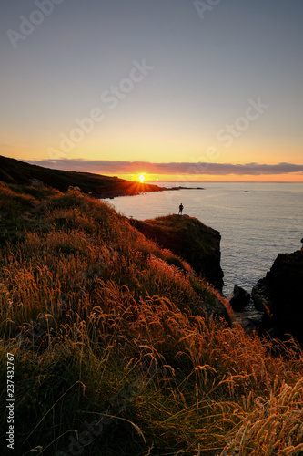 A lone figure standing on the cliff edge watching the sun go down on the South West coast path near St Ives in Cornwall